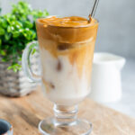 Side view of dalgona coffee in a glass cup with a straw