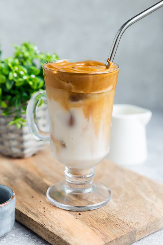 Side view of dalgona coffee in a glass cup with a straw