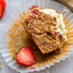 Top view of one half bitten keto strawberry muffin on a grey background